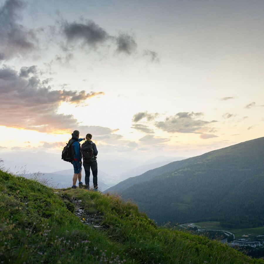 Zwei Wanderer stehen auf einem Berg und genießen den Blick bei Sonnenuntergang